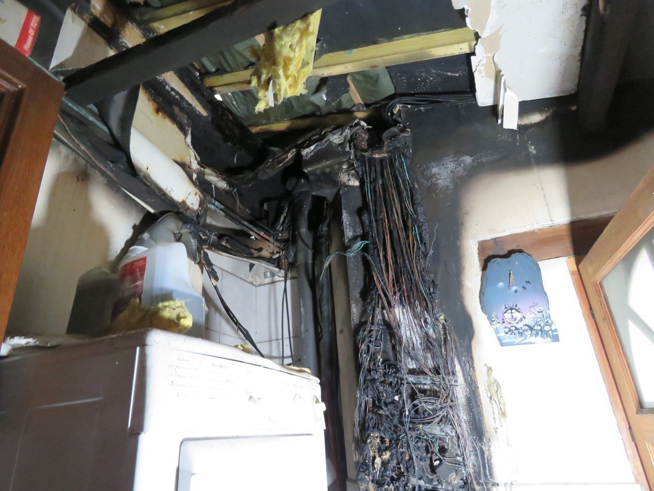 Dégâts d'un incendie d'origine électrique dans une buanderie : câbles brûlés, plafond noirci et isolant fondu